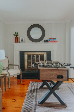 Une pièce avec une table de baby-foot, une cheminée, un miroir et une chaise.