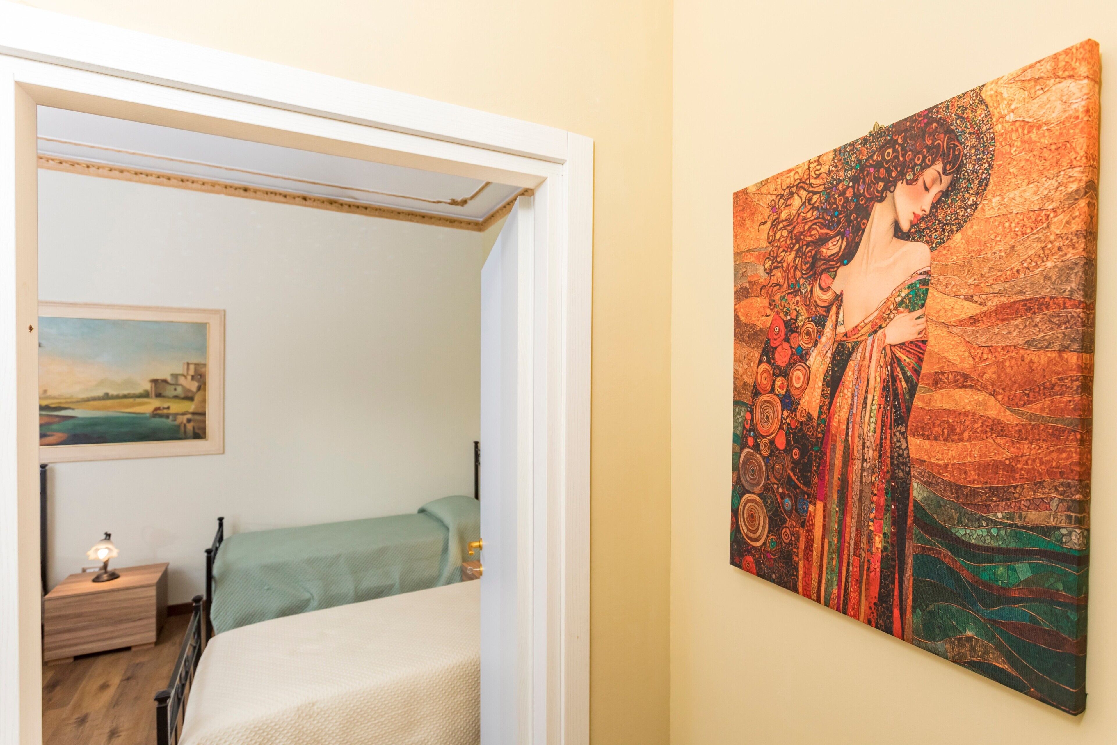 Camera da letto con un letto, un comodino, un quadro appeso e una porta che dà su un'altra stanza.