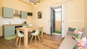 Een knus woongedeelte met kitchenette, eethoek en een bank met bloemenkussens.