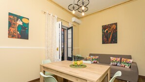 Een eetgedeelte met een houten tafel en stoelen, een bank met kleurrijke kussens, en twee schilderijen aan de muur.