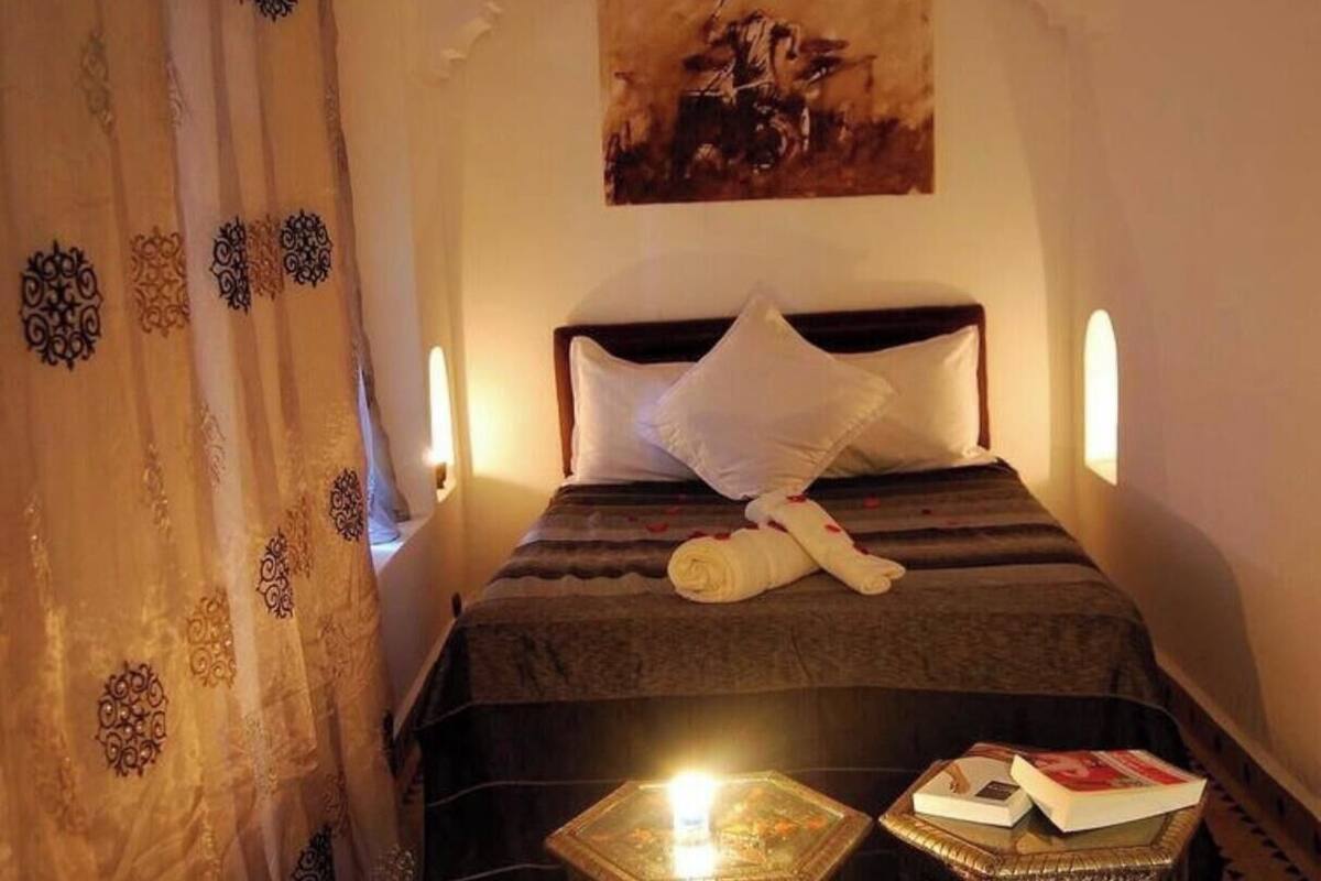 Uma cama com uma toalha enrolada, uma mesa de cabeceira com um livro e um quadro acima da cama.