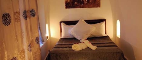 A bed with a rolled towel, a bedside table with a book, and a painting above the bed.
