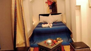 A bedroom with a bed, a small table with a candle, a book, and a decorative item.