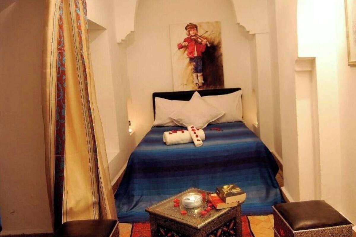 Quarto com uma cama, uma mesinha com uma vela, um livro e um objeto decorativo.