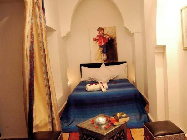 A bedroom with a bed, a small table with a candle, a book, and a decorative item. - Hotel Riad hannah (Marrakech)