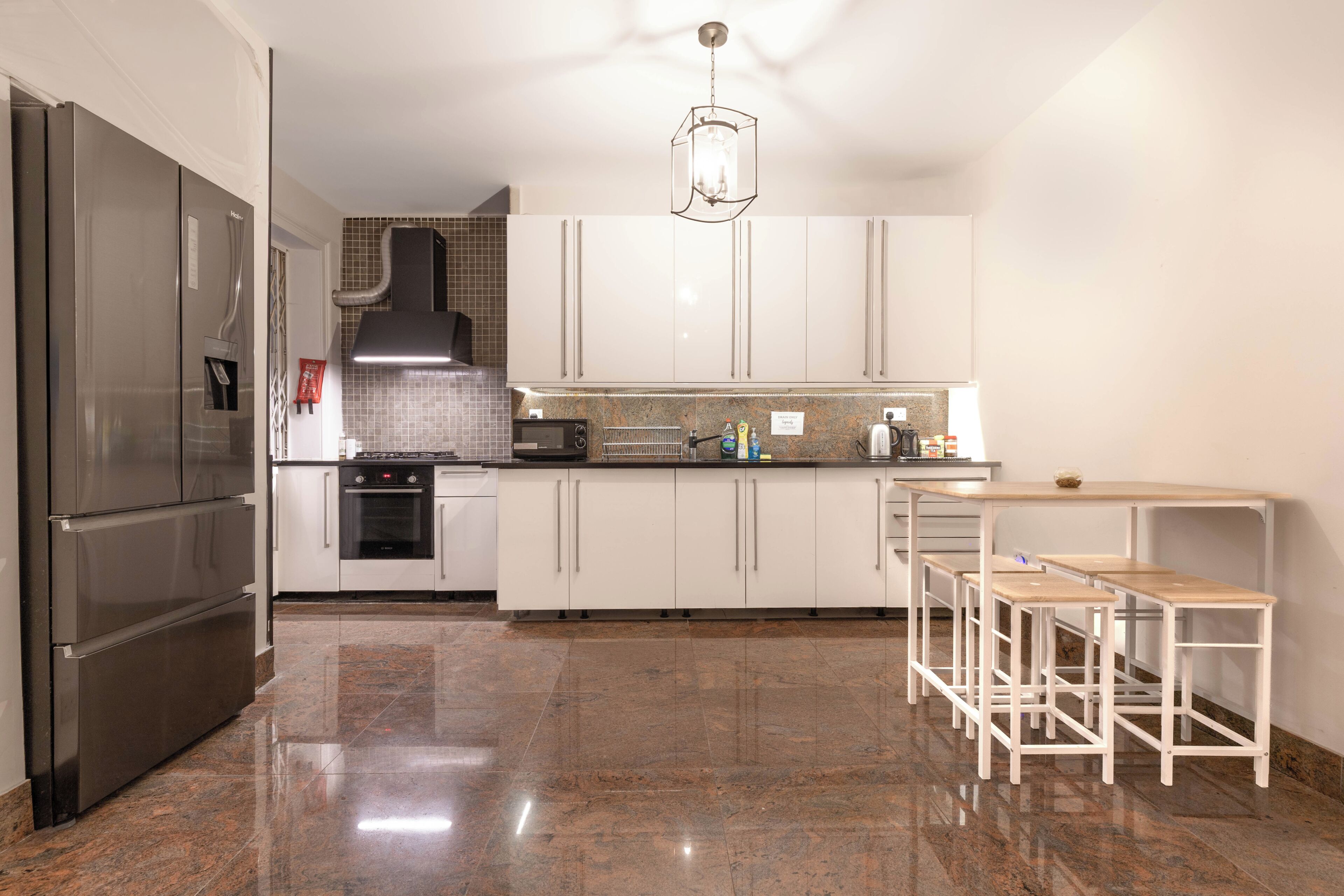 A modern kitchen with stainless steel appliances, white cabinets, a tiled backsplash, and a bar area with stools.
