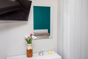 A bathroom with a white vanity, a vase with flowers, a heart-shaped decoration, and a mirror reflecting a teal-colored wall.