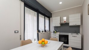 Een moderne keuken met witte kastjes, een zwarte oven en een eethoek met een tafel en stoelen.