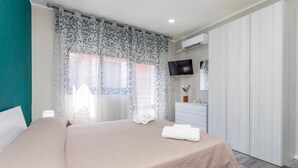 Een slaapkamer met een bed, een televisie, een kast en een raam met gordijnen.