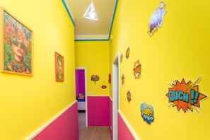 A brightly colored hallway with yellow walls, pink lower half, and various wall decorations including comic-style stickers.