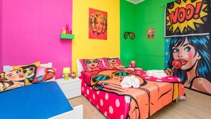 A brightly colored room with a bed, pillows, and wall art.