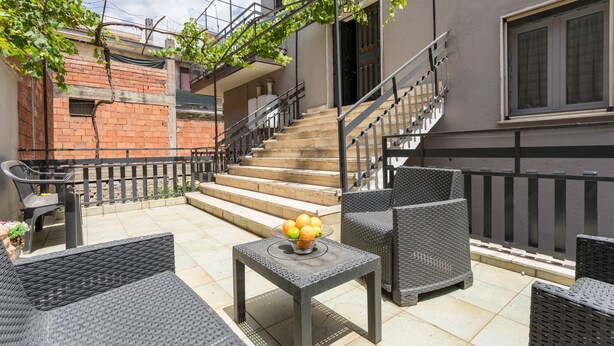 A patio with wicker furniture, a table with fruit, and a staircase leading to an upper level.