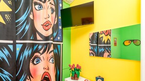 A brightly colored room with a white dresser, a flat-screen TV, and artwork on the walls.