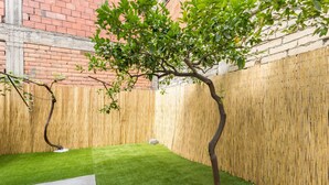 A small backyard with artificial grass, a tree, and a bamboo fence.