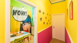 A brightly colored room with a door, a wall with comic book-style decorations, and a table with a bowl of fruit.
