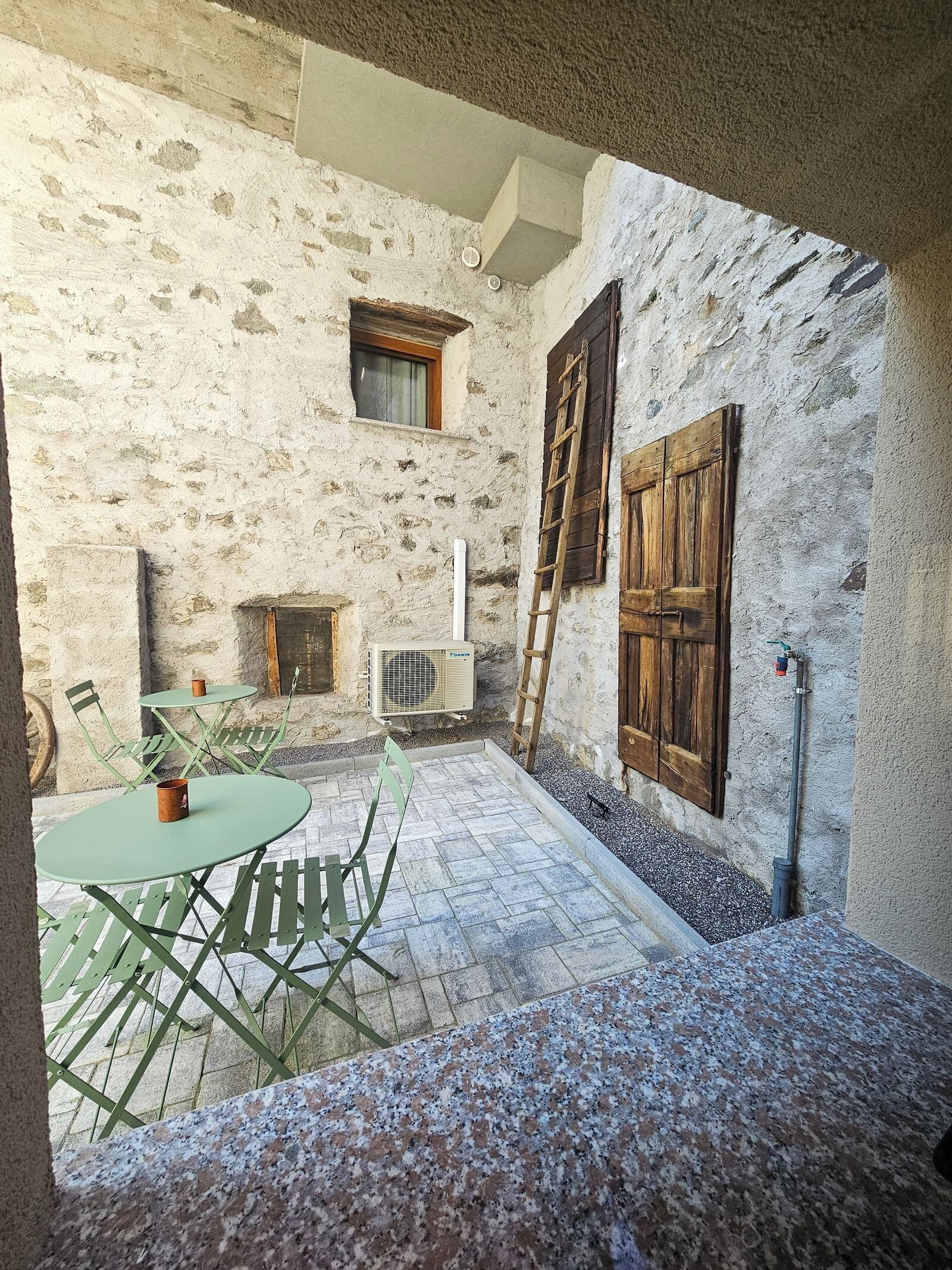 A rustic stone interior with a stone floor, a wooden door, a window, and a small table with chairs.