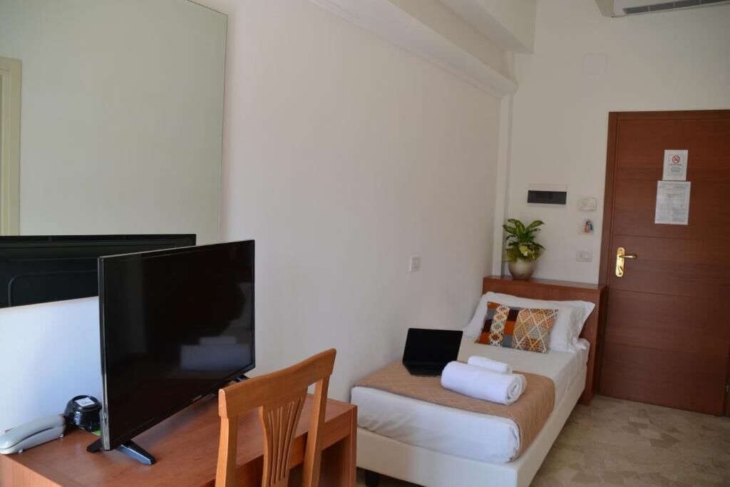 A hotel room with a bed, a desk with a computer, a chair, a television, and a door.