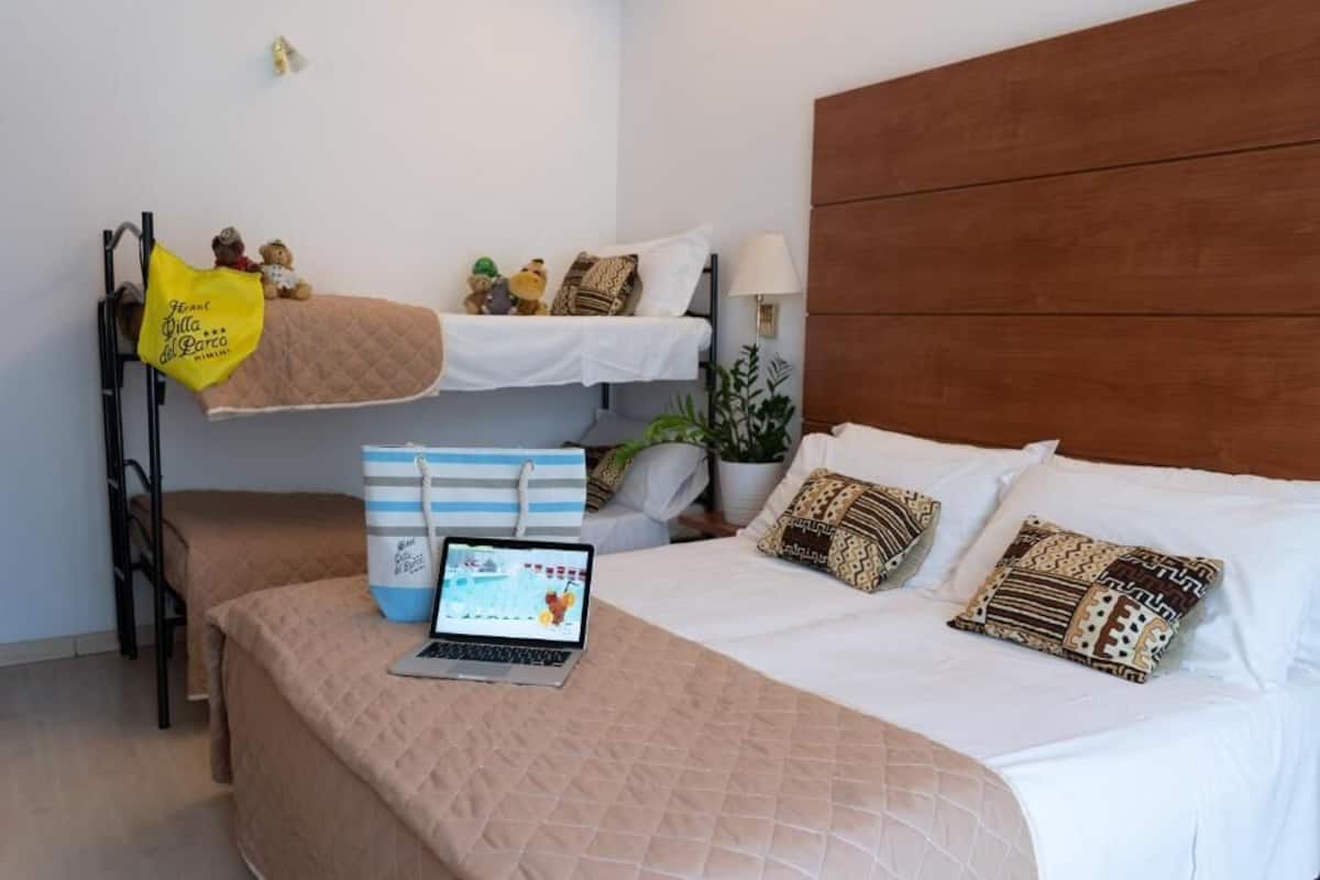 Habitación de hotel con literas, un escritorio con una computadora portátil, una mesita de noche y una lámpara.