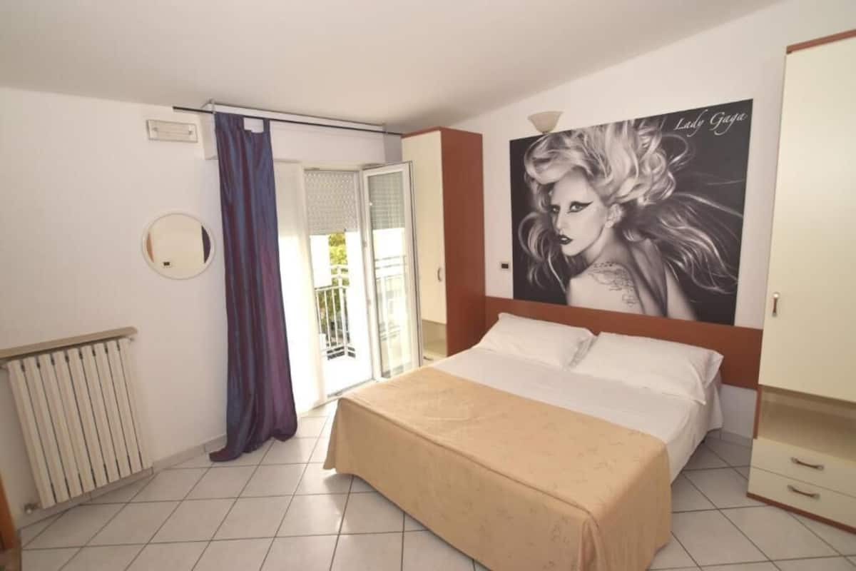 Un dormitorio con cama, un radiador, una ventana con cortinas y un cartel en la pared.