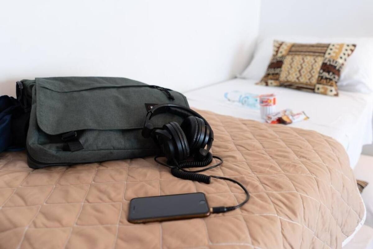 Una cama con una colcha acolchada, un teléfono inteligente negro y una bolsa gris con auriculares.