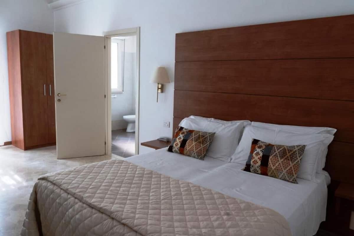 Un dormitorio con una cama grande, un armario de madera y un baño visible a través de una puerta abierta.