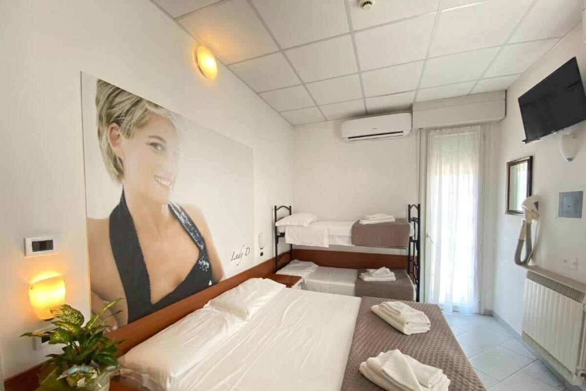 Una habitación de hotel con una cama grande, una cama más pequeña, una mesita de noche con una planta, un televisor montado en la pared y un equipo de aire acondicionado.