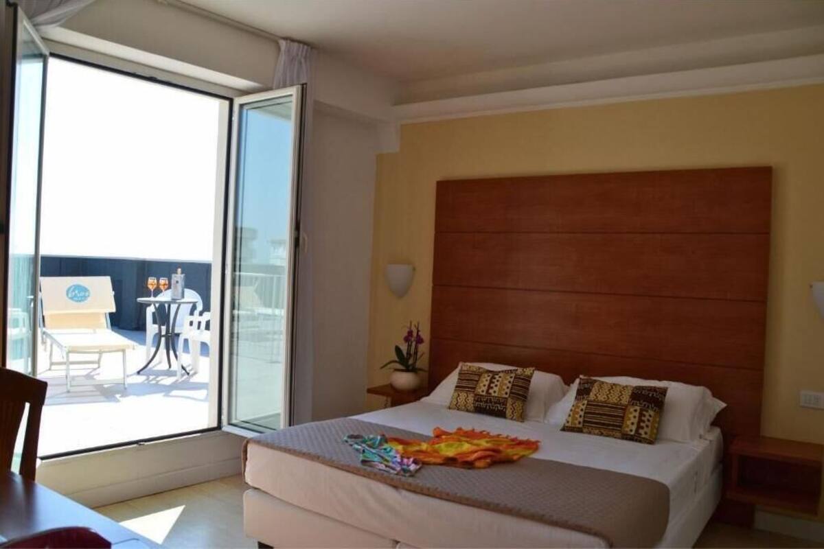 Habitación de hotel con una cama, una mesita de noche, una ventana con vistas al exterior y una pequeña mesa con sillas.