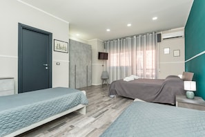 A bedroom with two beds, a TV, and a grey chair. - Etnamia Apartment - 2 (Paterno)