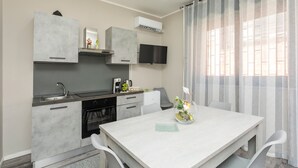 Een moderne keuken met een eethoek, een flatscreen televisie en een groot raam met gordijnen.