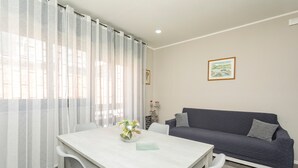 Een woonkamer met een bank, een eettafel met stoelen en een raam met gordijnen.