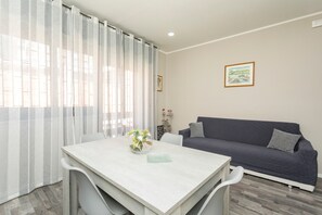 A living room with a sofa, a dining table with chairs, and a window with curtains. - Etnamia Apartment - 2 (Paterno)