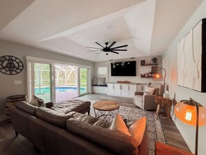 A spacious living area with a large sofa, a coffee table, and a TV mounted on the wall. - Luxury 4 Bedroom Family Pool Home (Stuart)
