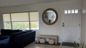 A living room with a dark blue sofa, a round mirror, a wooden bench, a white door, and a potted plant. - Peaceful and updated 4-bedroom house in East Quogue (East Quogue)