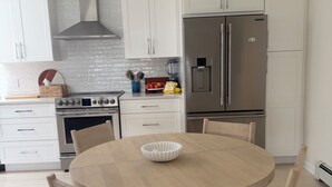 A modern kitchen with white cabinets, stainless steel appliances, and a round wooden dining table with chairs. - Peaceful and updated 4-bedroom house in East Quogue (East Quogue)