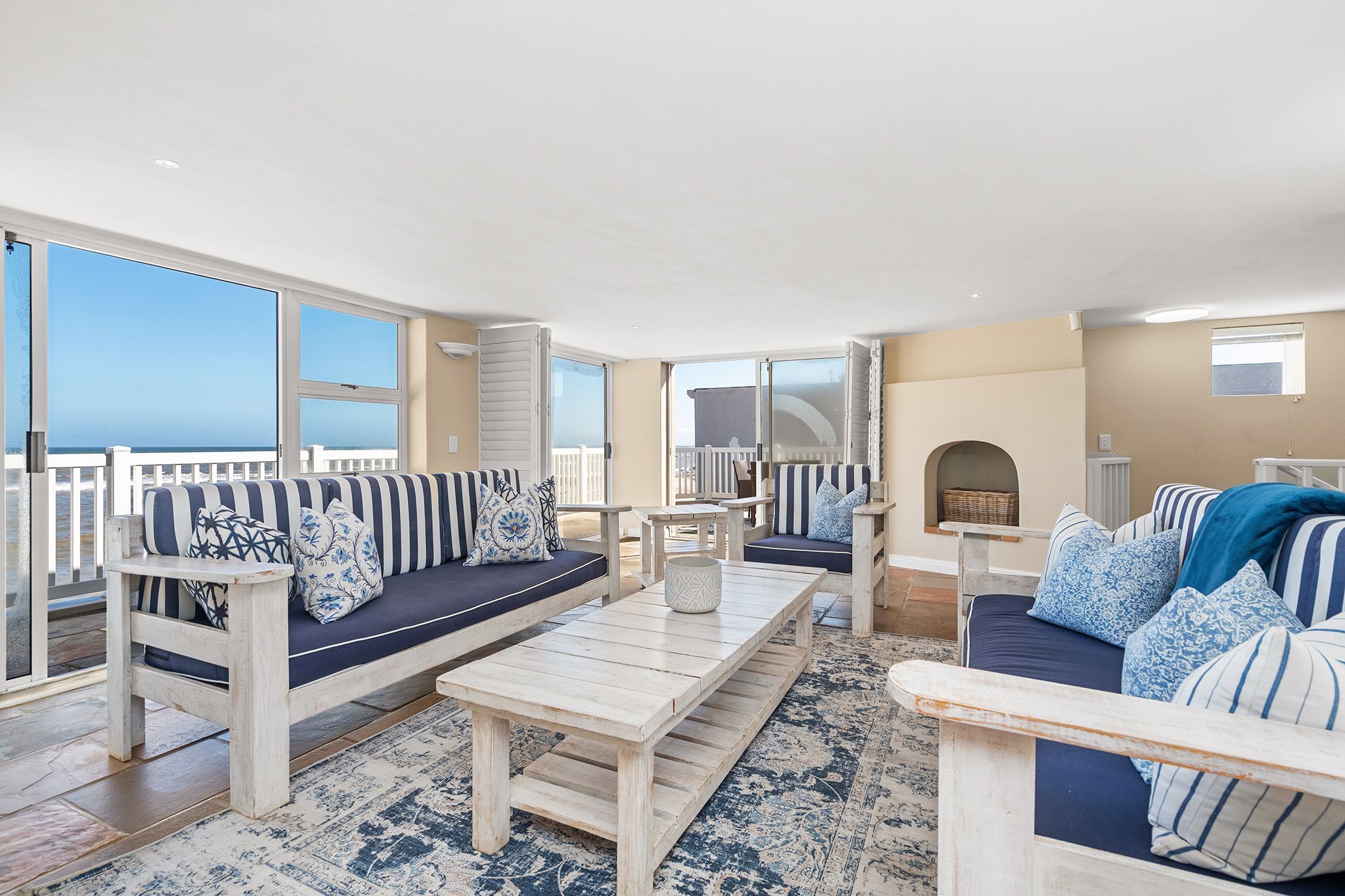 A spacious balcony with a view of the ocean, a wooden coffee table, and striped sofas with cushions.