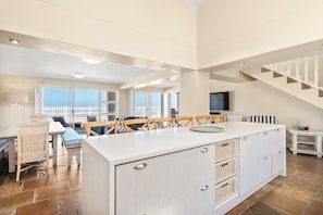 A spacious kitchen with a large island, wooden chairs, and a view of the sea through large windows. - Sea Haven 4 (Cape Town)