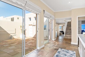 Un interior amplio con un gran ventanal corredera que da a un patio exterior, una escalera y una zona de cocina.
