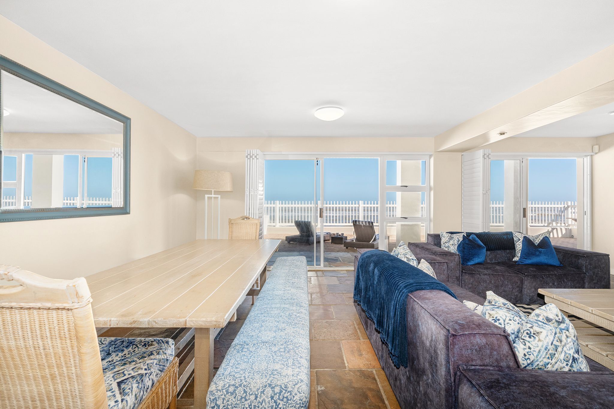 A spacious room with a large dining table, a sofa set, and a view of the sea through large windows.