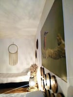 A bedroom with a bed, a wall-mounted dreamcatcher, a framed artwork, and a decorative vase.