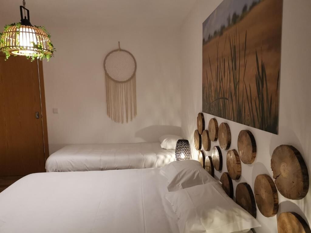 Une chambre avec deux lits, un luminaire suspendu, un attrape-rêves et une œuvre d’art en bois fixée au mur.