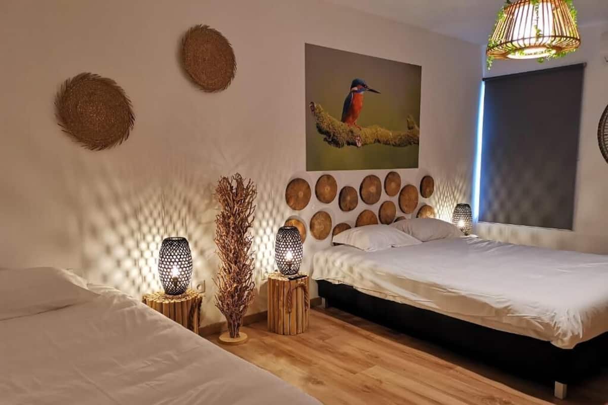 Un dormitorio con dos camas, una obra de arte en la pared de un pájaro y una lámpara colgante.