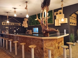 A bar area with a central wooden tree sculpture, a sign reading 'BEM VINDO,' and multiple stools.