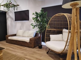 A room with a wicker sofa, a hanging chair, a potted plant, and a lamp.