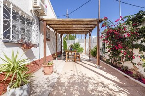 Eine überdachte Terrasse mit Tisch, Stühlen, Blumentöpfen und einer Wand mit Kletterpflanzen.