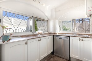 Una cocina con armarios blancos, un lavavajillas de acero inoxidable y un ventanal con detalles de hierro forjado.