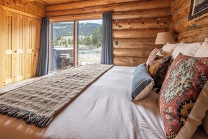 Ein Schlafzimmer in einer Blockhütte mit einem Bett, Kissen, einem Teppich und Blick ins Freie.