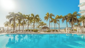 A swimming pool with lounge chairs and palm trees, a beach in the background, and a building with balconies. - Santo Domingo Bay (Boca Chica)