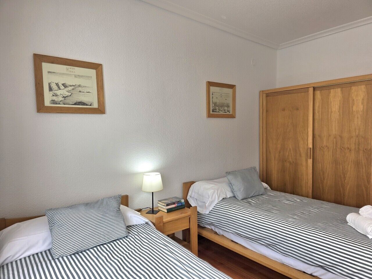 Une chambre avec deux lits, une armoire en bois et deux tableaux encadrés accrochés au mur.