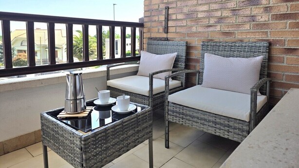 Un balcon agrémenté de meubles en osier, d’une machine à café et d’un plateau avec des tasses et une théière.