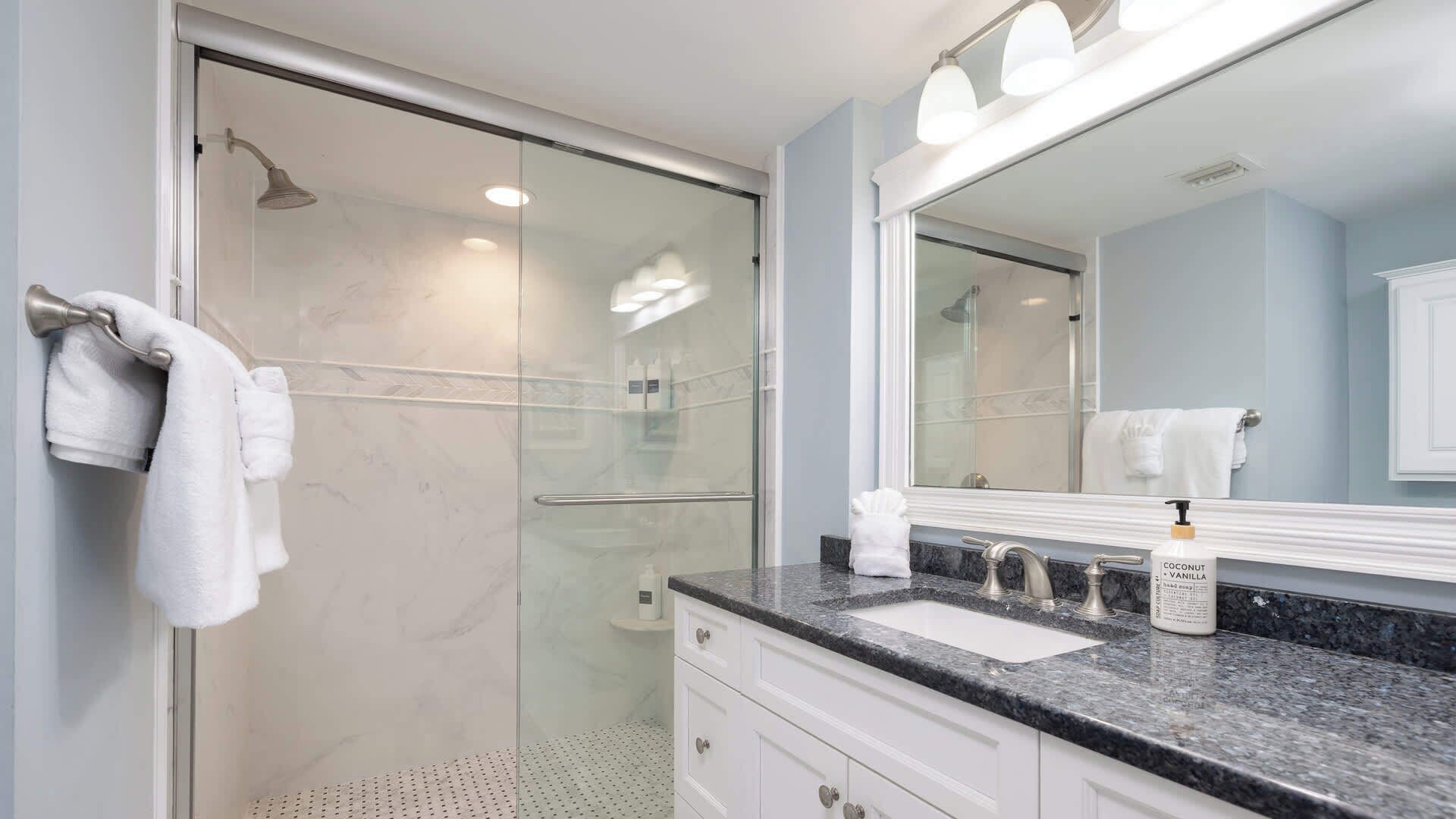 A modern bathroom with a glass shower enclosure, a sink with a vanity, and a large mirror.